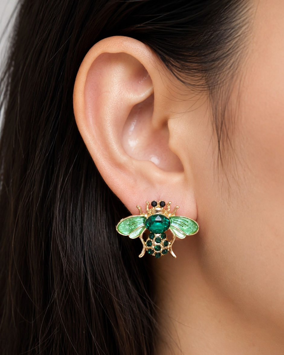 Close-up of an ear wearing a green insect-shaped earring with a blurred background